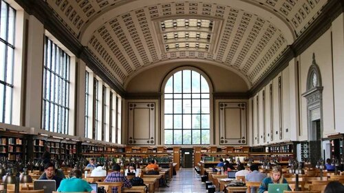 Inside of the UC Berkeley library, featuring a center aisle between long tables with students working at them